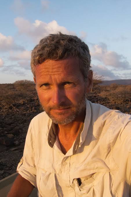 a person wearing a beige shirt the sky and clouds behind him