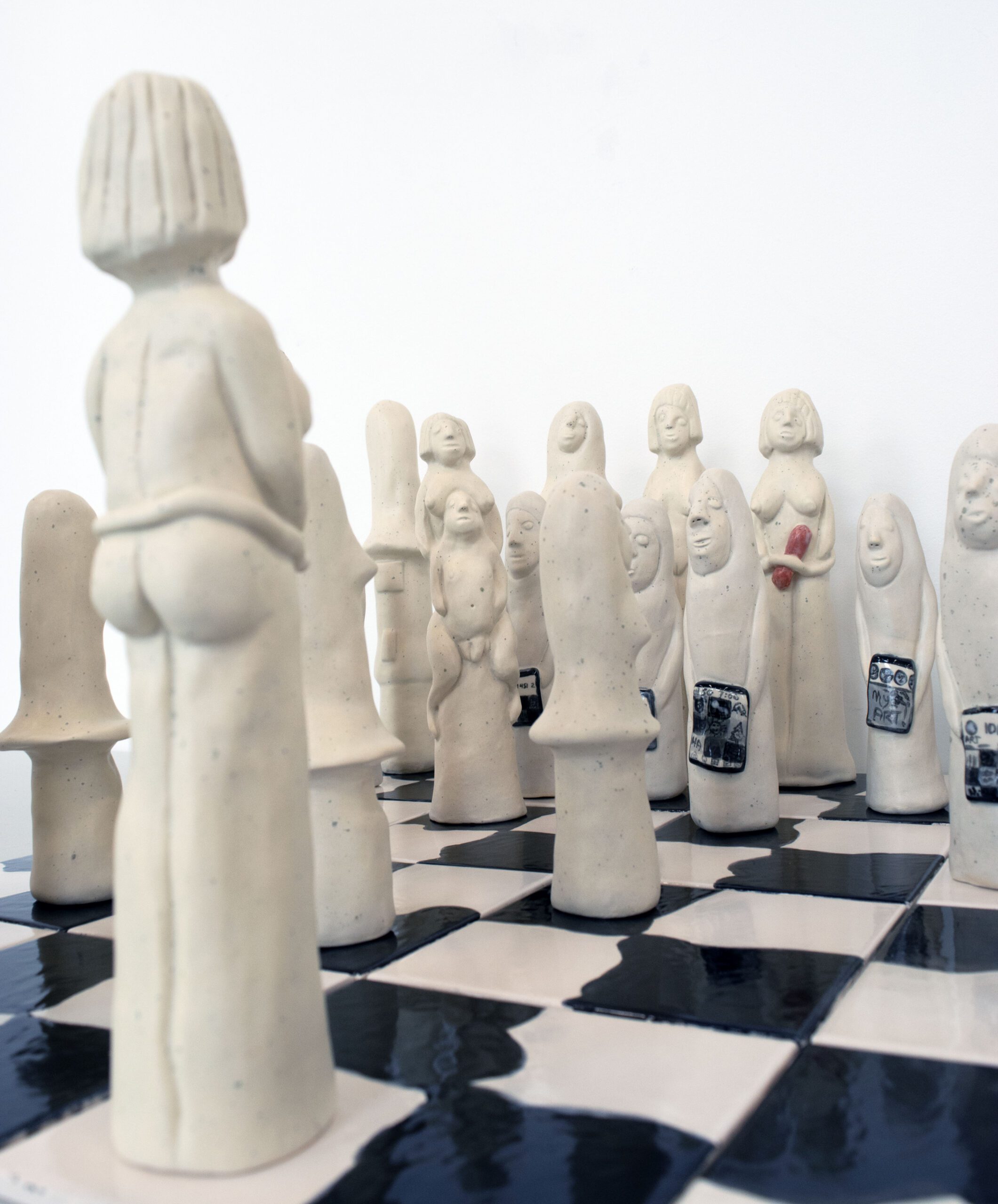 Close-up of ceramic chess pieces with unique human-like forms on a chessboard.