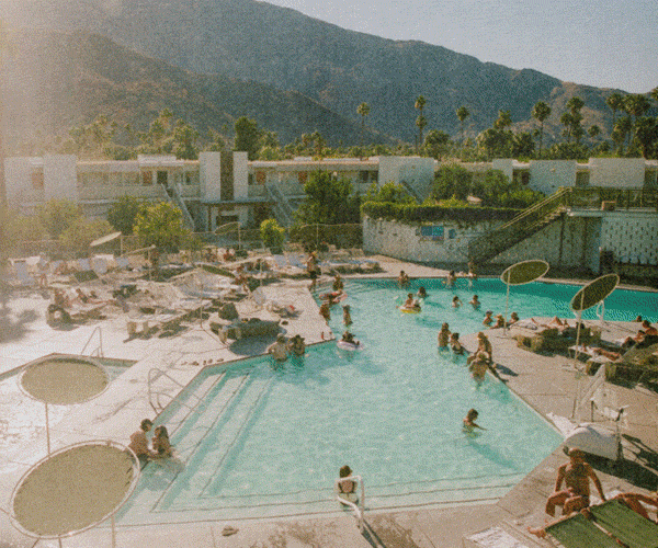 Guests enjoying a sunny day by the pool at Ace Hotel & Swim Club Palm Springs, surrounded by mountains and palm trees in the background.