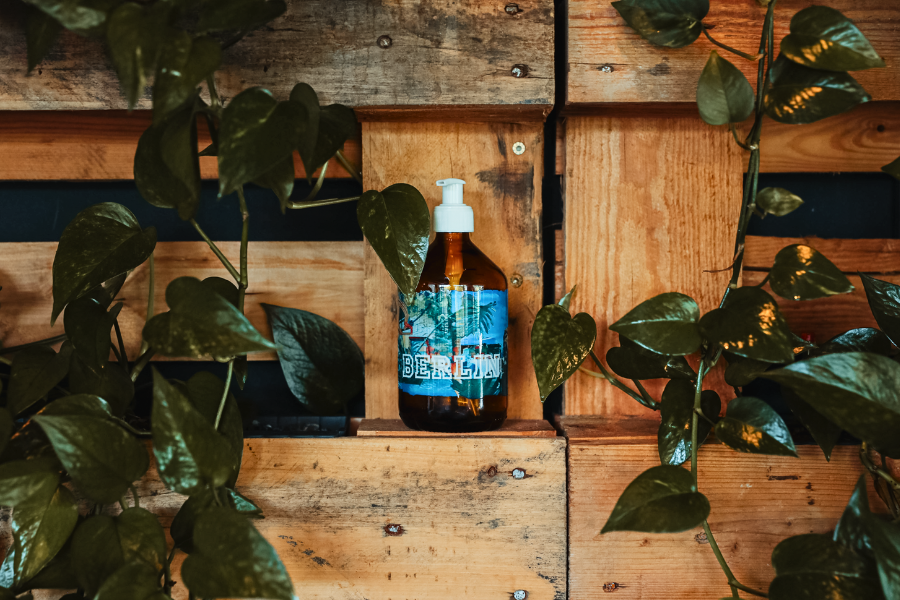 Soeder soap bottle with illustration by Studio Aisslinger, in front of a wall of wooden pallets and green plants