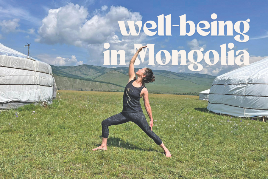 A woman practices yoga on a grassy plain between two traditional huts in Mongolia