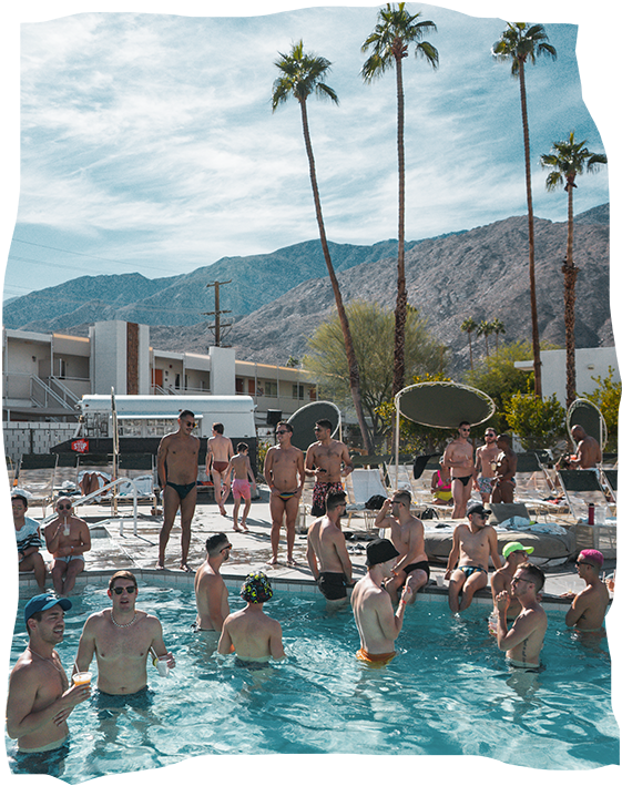 A sizable gathering of men reveling in a sunlit pool celebration in Palm Springs, with palm trees setting the backdrop, in honor of Palm Springs Pride.